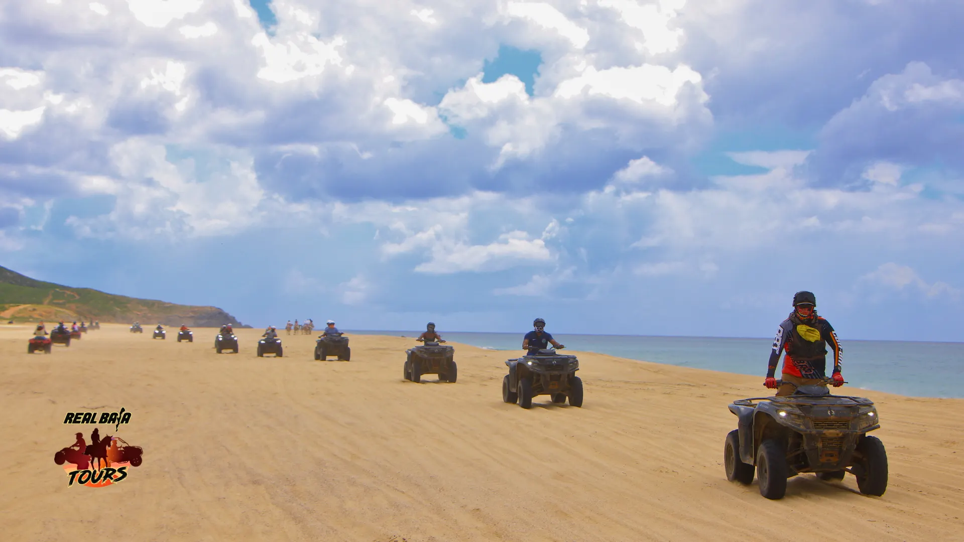 Group of ATV riders on a sandy beach in Baja California Sur with ocean and cloudy sky