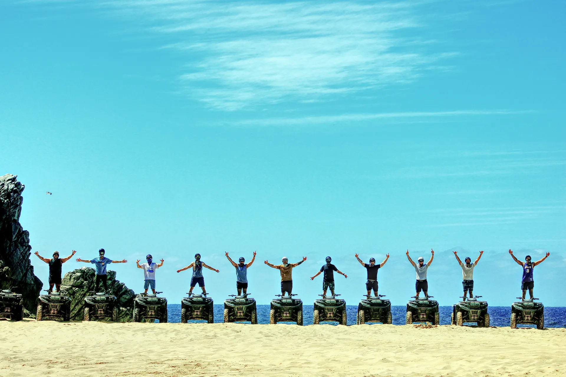 Group of tourists with arms raised celebrating on wooden posts at beach in Migrino Cabo San Lucas Real Baja Tours