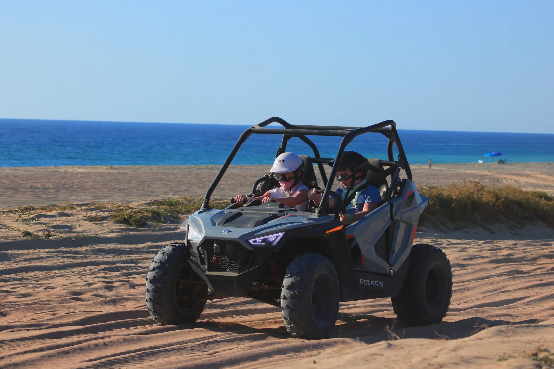 Polaris RZR buggy with two passengers on sandy beach with ocean and blue sky in Baja California Sur