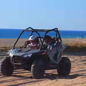 Polaris RZR buggy with two passengers on sandy beach with ocean and blue sky in Baja California Sur