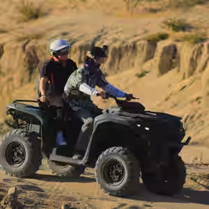 Two riders on black Double ATV exploring sandy desert terrain with eroded canyon walls in Baja California Sur